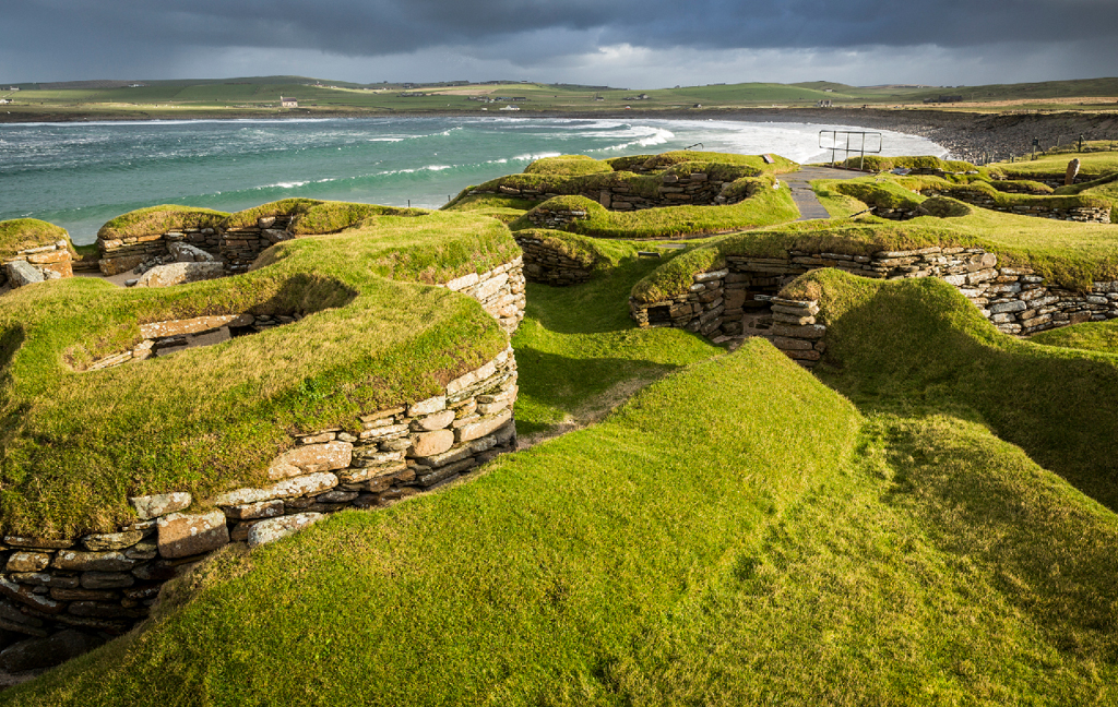 Stone-built Neolithic structures covered with grass in a coastal landscape beside the sea