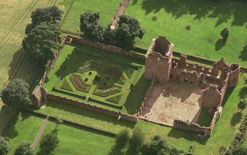 Aerial view of Edzell Castle showing its walled Renaissance garden with geometric parterres, clipped hedges and a central mound, beside the red‑sandstone castle ruins and surrounding green fields.