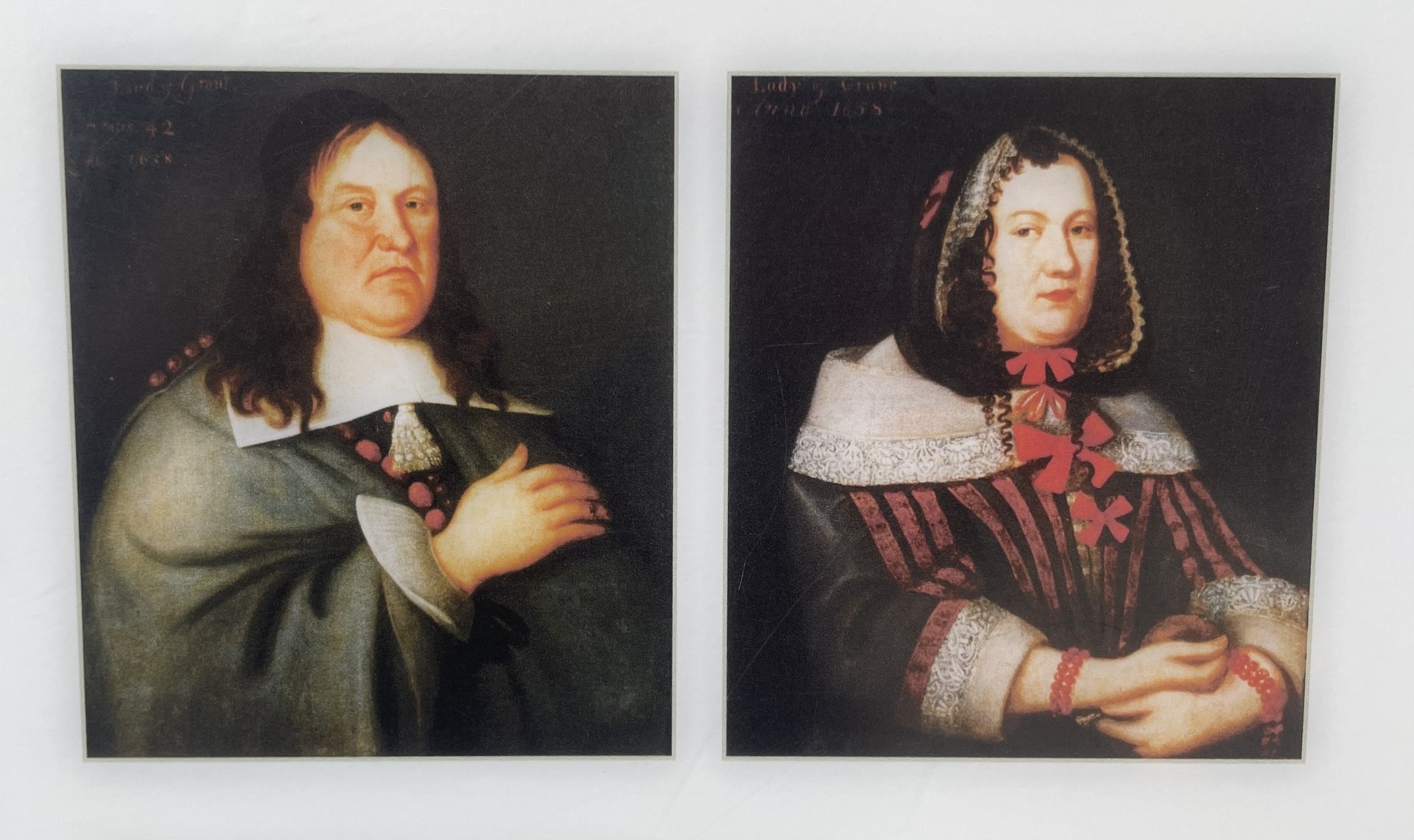 A pair of old painted portraits displayed side‑by‑side, showing individuals in period clothing with ornate details, one wearing a dark cloak with lace collar, the other in richly patterned garments with decorative trim.