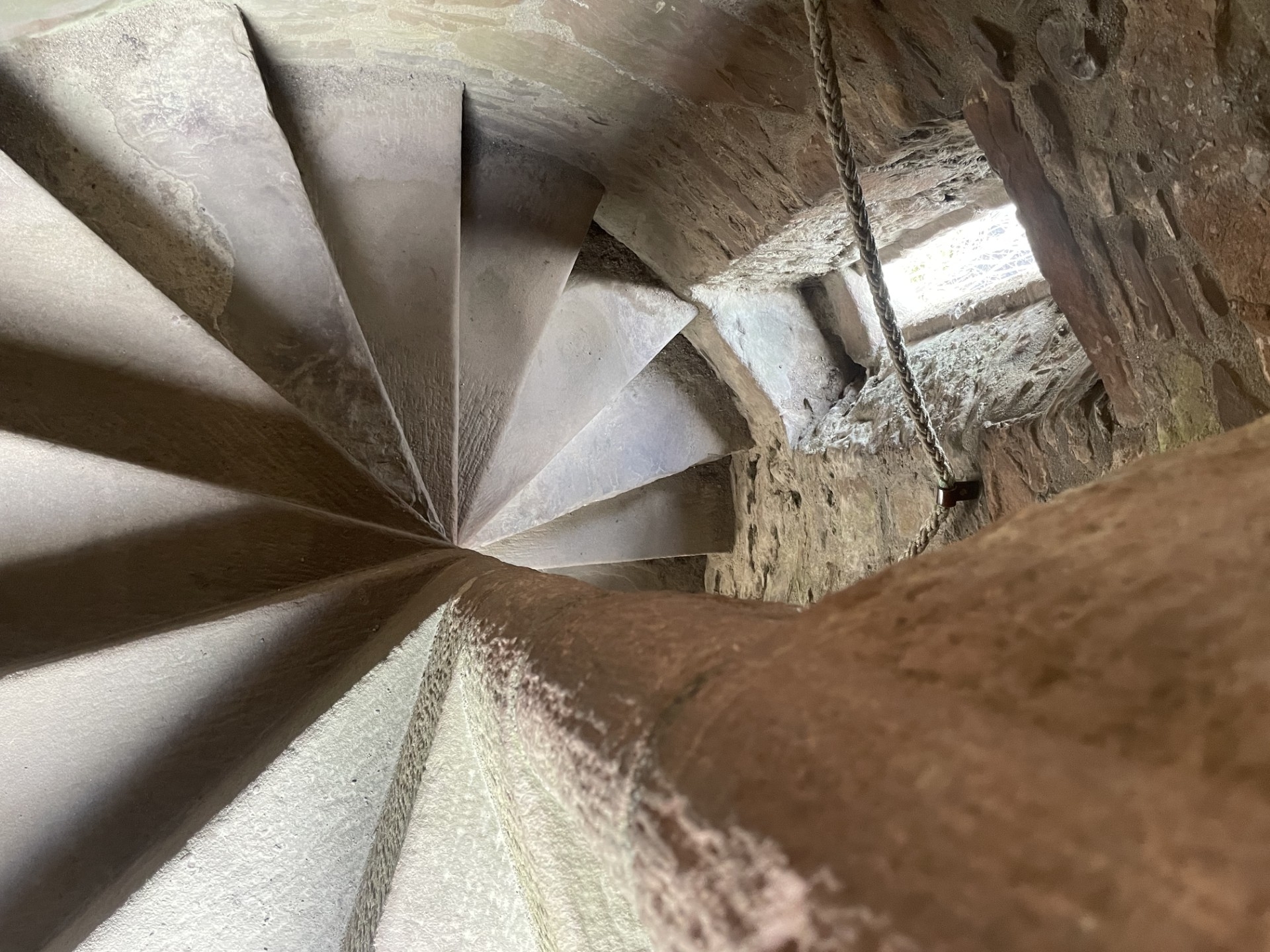 A narrow stone spiral staircase inside the castle, lit by daylight coming through a small window in the wall.