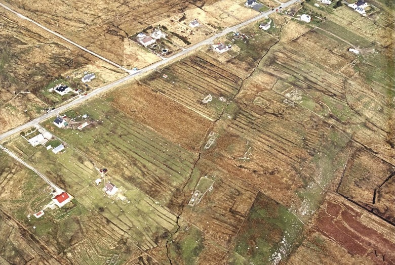 Aerial view of Achmore village showing scattered houses along a main road, surrounded by patchwork fields and moorland with long rectangular crofting plots.