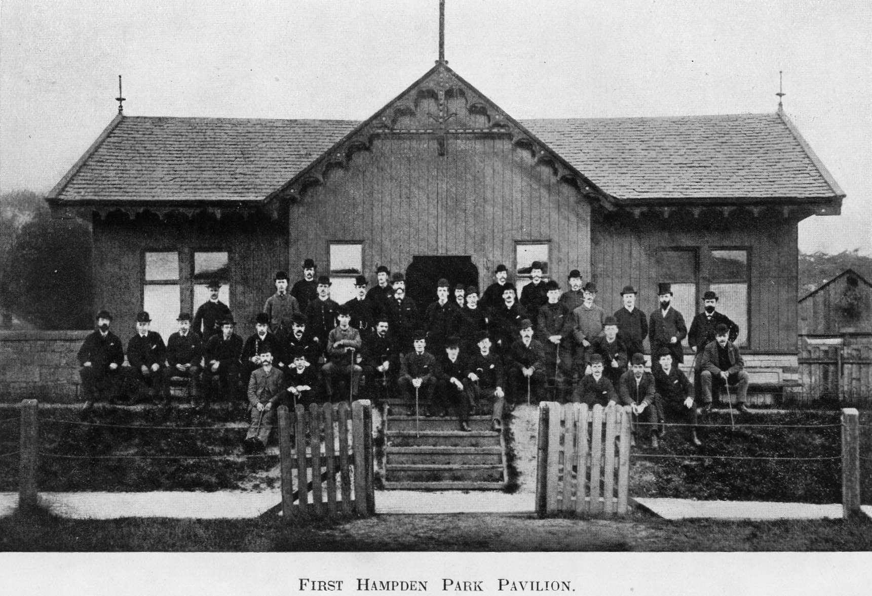Monochrome archive image of men standing outside a pavilion. 