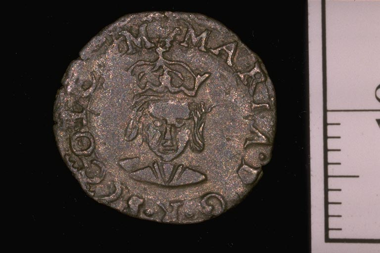 Historic coin featuring a woman wearing a crown against a black background with a ruler beside it.