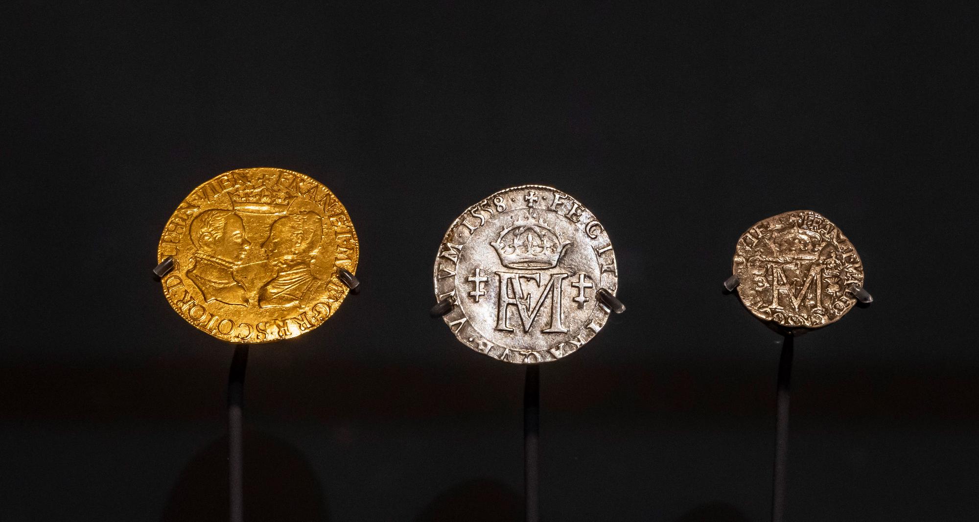 Three historical coins on display against a black background. 