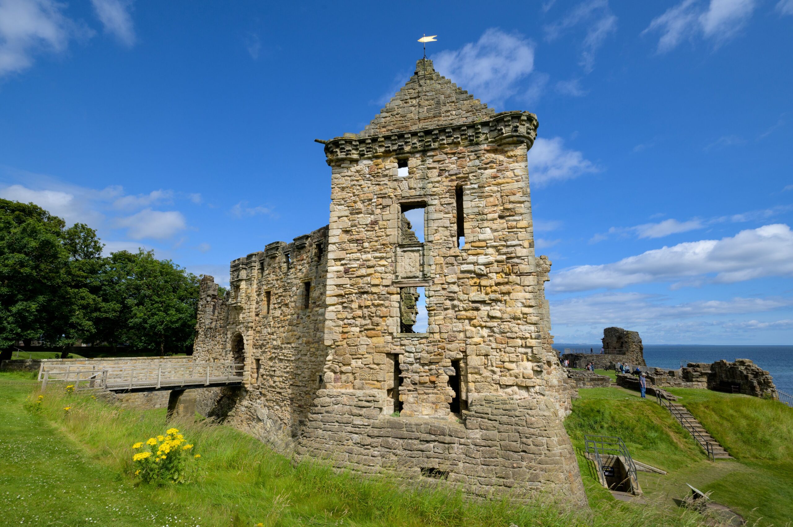 Castle ruin with green grass at the front under a blue sky on a sunny day.
