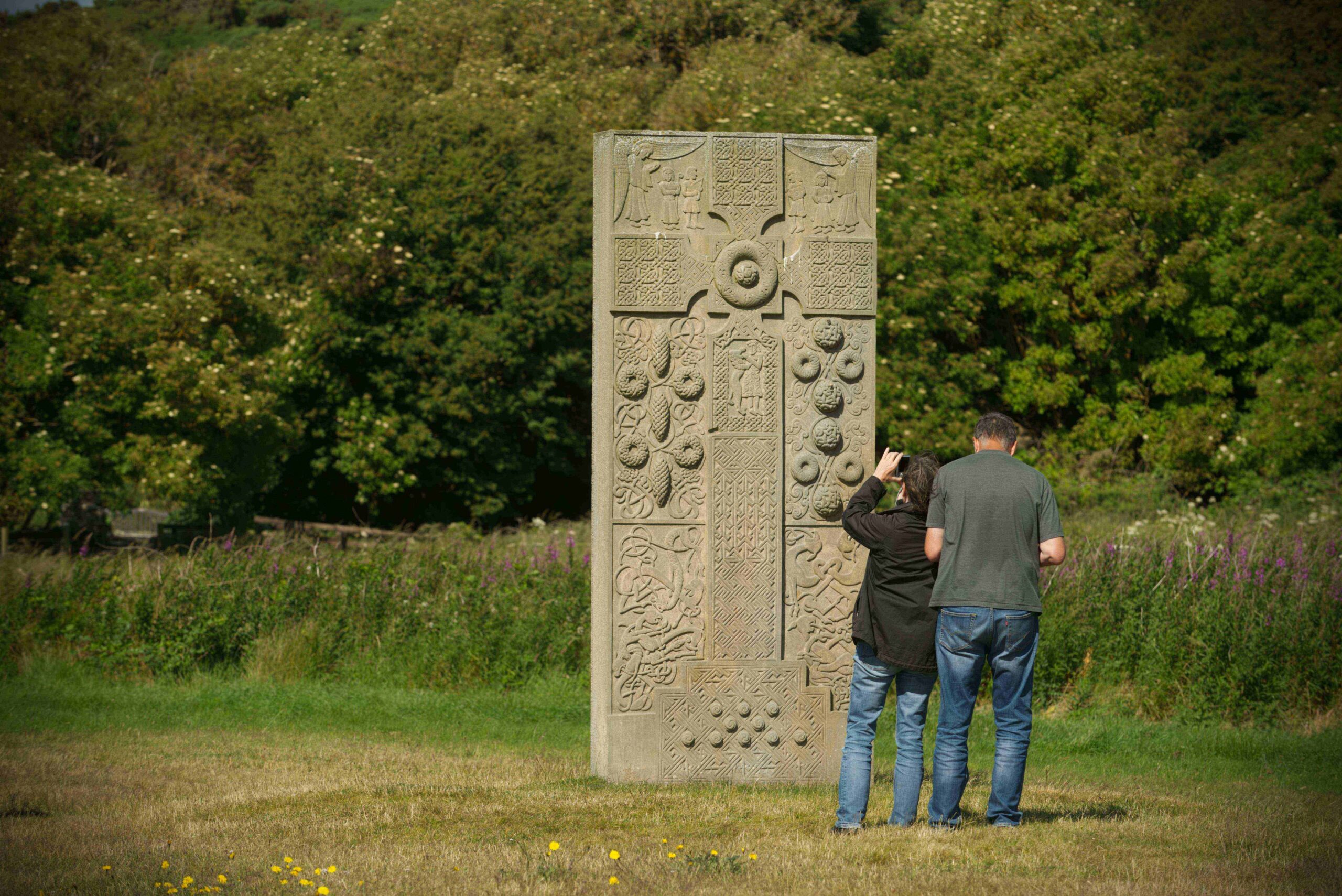 People looking at a Pictish stone in a green landscape.