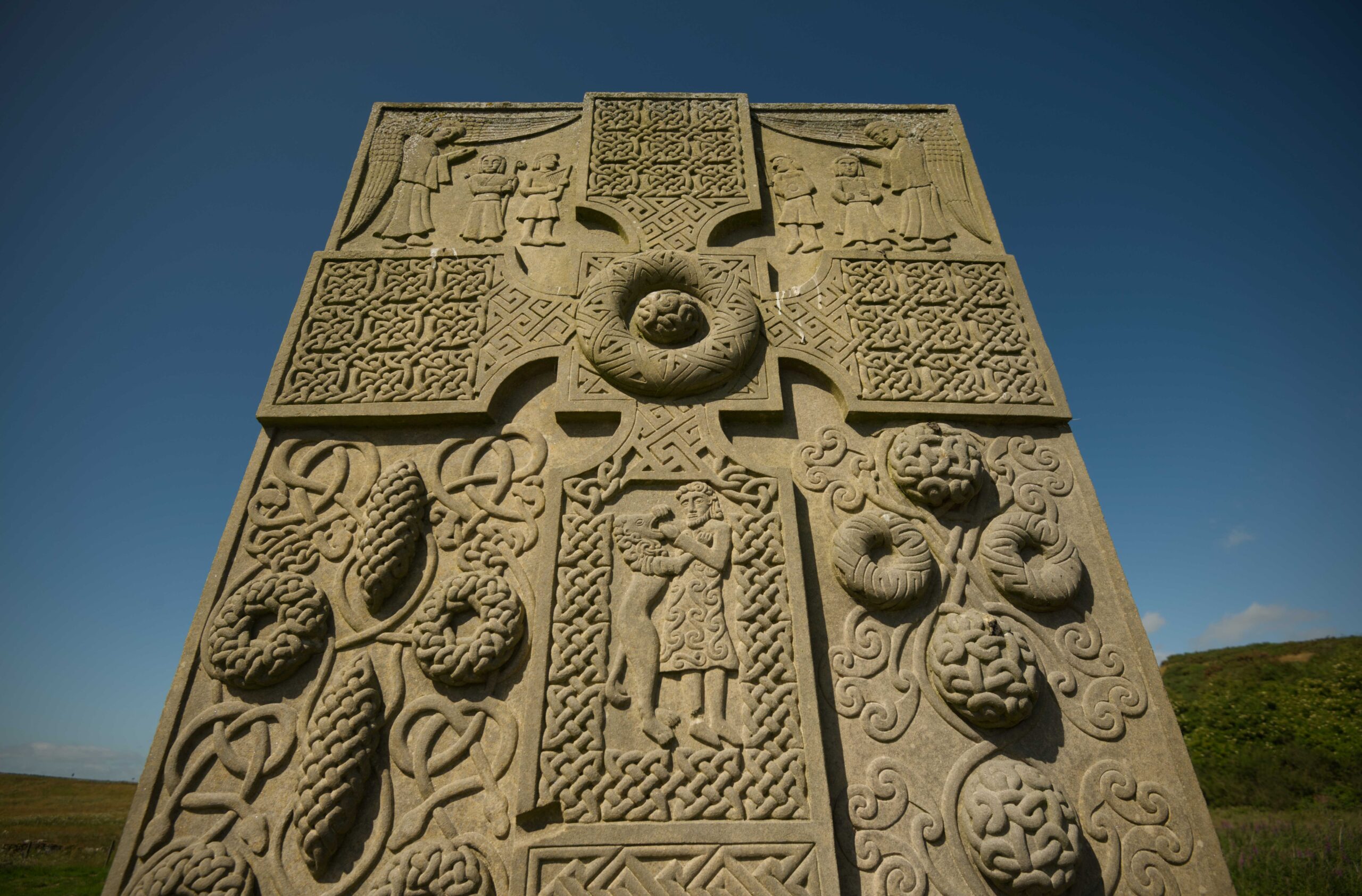 Close up of a carved Pictish stone with blue sky and green grass in the background. 