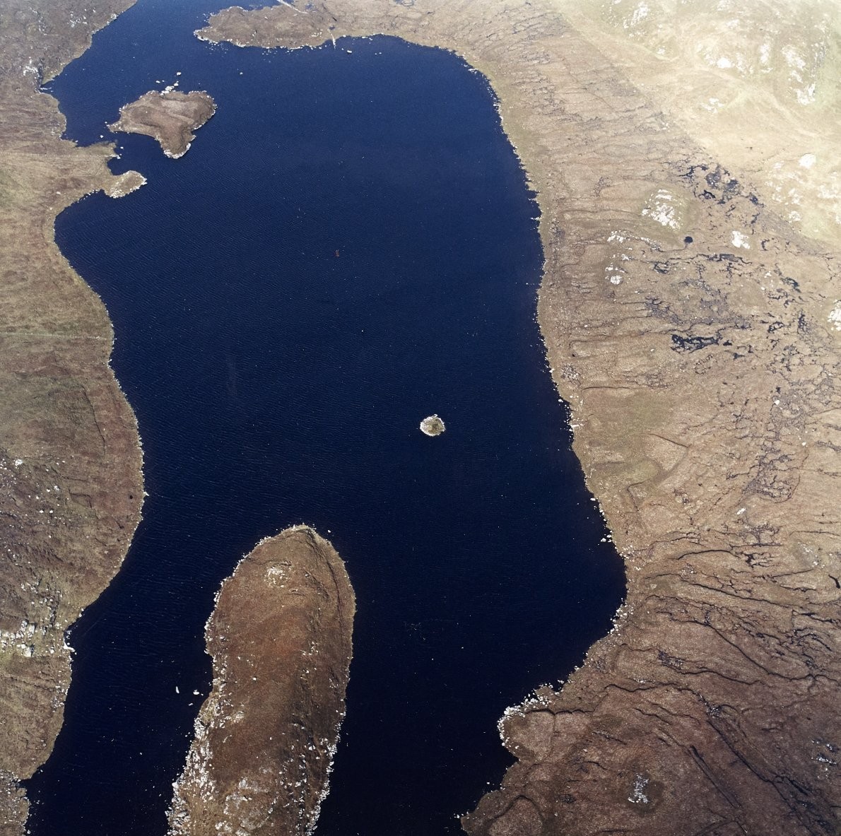 Oblique aerial view centred on the remains of a crannog on a loch.